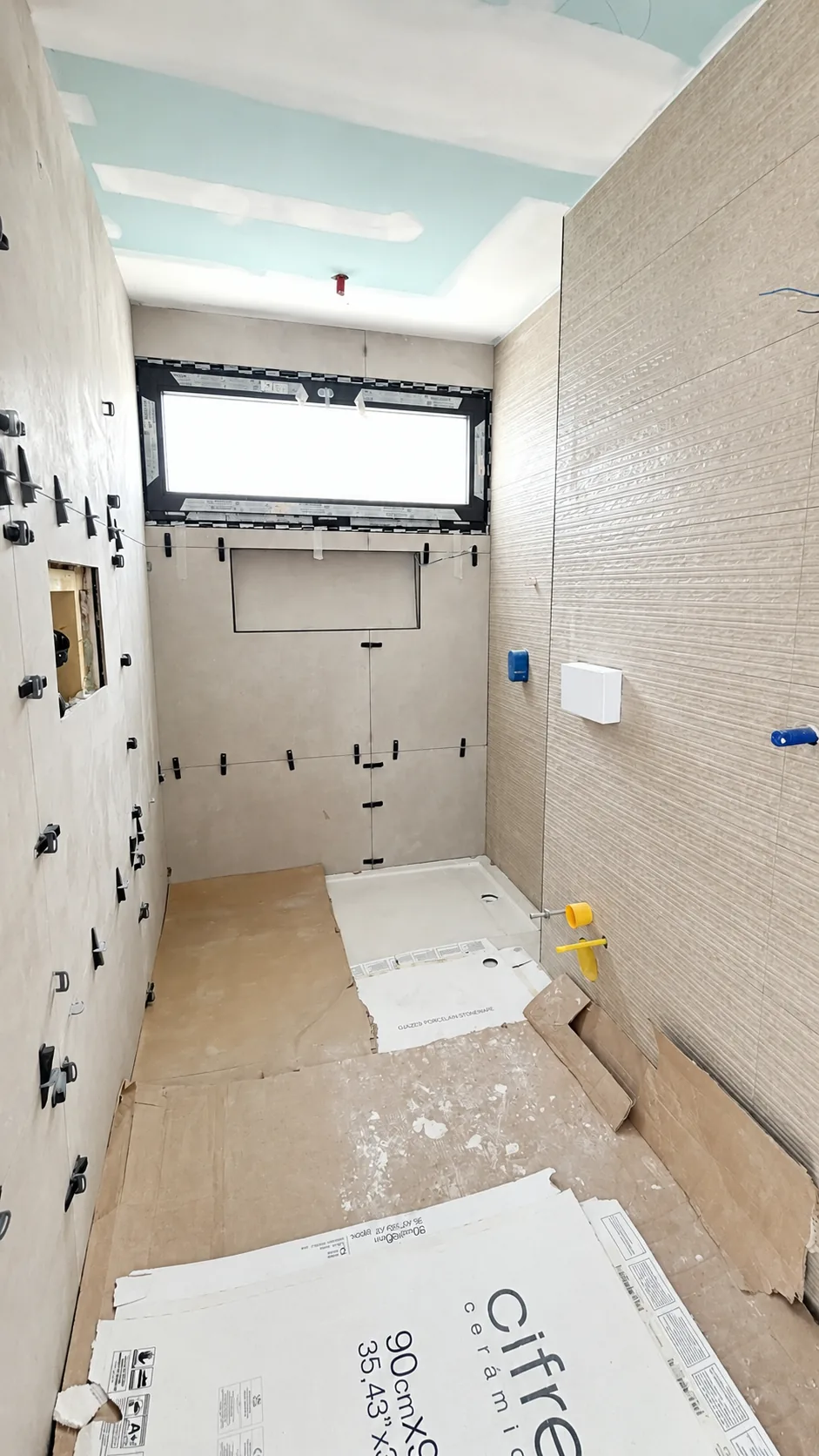 Baño en fase de obra, con alicatado en curso, instalaciones vistas y plato de ducha colocado.
